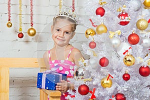 A girl stands at a Christmas fir-tree with gift in hand