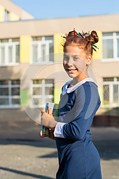Girl stands with classbook near a school and smiles