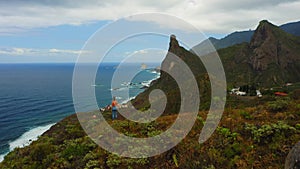 Girl stands on cliff edge with deep ocean mountain range aerial view on cloudy day. Green coastline. Rock of the Souls