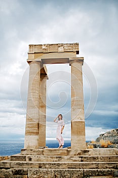 A girl stands between the columns of the Acropolis in Lindos, Rhodes, Greece.