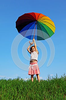 Girl stands on green grass with colored umbrella