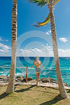 Girl stands with her back against the blue ocean between palm trees. Cancun Mexico