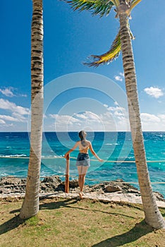 Girl stands with her back against the blue ocean between palm trees. Cancun Mexico