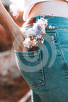 The girl stands with her back in blue jeans, flowers in her back pocket