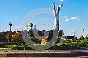 A girl stands on her hands upside down on a square in the city center.