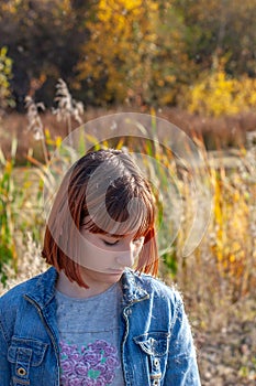 A girl stands with her head bowed on a sunny day against the backdrop of an autumn forest