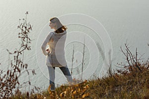 A girl stands on a hill by the sea and looks around, rear view