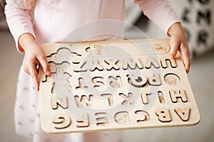 A girl holds in her hands a children`s wooden alphabet.