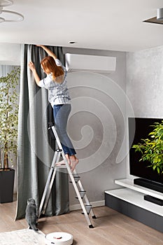 The girl stands on a ladder and hangs curtains. The concept of repair, relocation