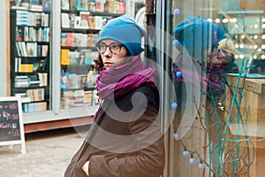 Girl stands leaning to a window of a shop at the shopping street