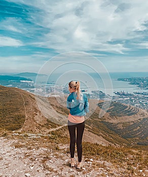 A girl stands on a mountain and looks at the sea.