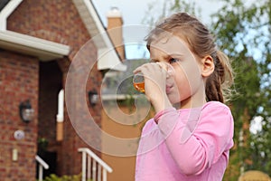 Girl stands near cottage and drinks juice