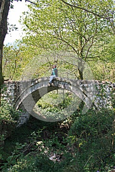 A girl stands on an old antique bridge in the forest, Georgia, village of Mirveti