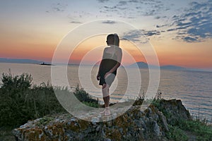 Girl stands on a rock and looks at the beautiful view of the sea and sunset