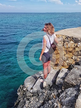 Girl stands on rocks, rocks and looks at the Caribbean Sea