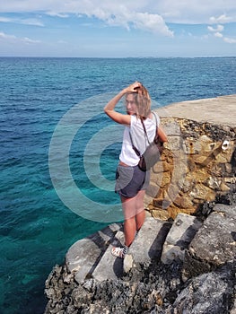 Girl stands on rocks, rocks and looks at the Caribbean Sea