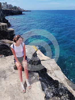 Girl stands on rocks, rocks and looks at the Caribbean Sea