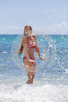 Girl stands in seawater, surrounded by a spray of seafoam