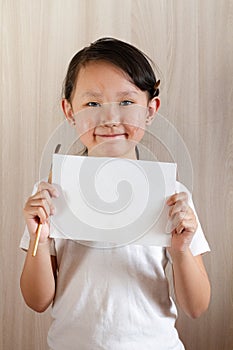 Girl stands with a sheet of white paper in her hands and a brush behind her ear