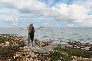 A girl stands on the shore of the Mediterranean Sea with her arms spread wide