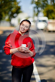 A girl stands smiling with a cup of coffee on a blurred background