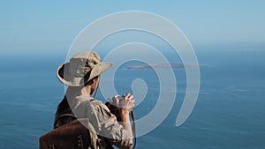 a girl stands on a table mountain and takes a photo of Robben Island, prison