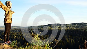 A girl stands on top of a mountain with her hands open. Freedom in the gesture.