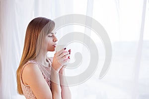 Girl stands at the window with a mug