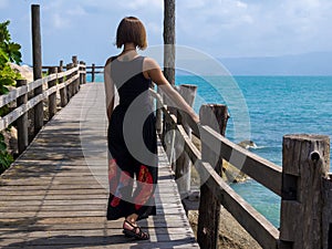 A girl stands on a wooden pier and looks at the sea