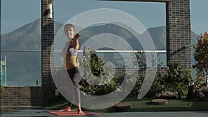 Girl stands in yoga on roof terrace against hills