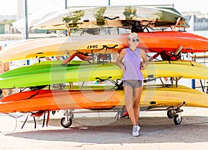 Girl stanfs in front of a pile of kayaks and canoes ready to sail in the sea.