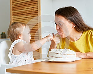 Girl sticking finger to mother. Trying cream from cake. Mother smiling and licking finger