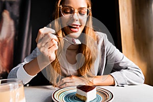 Girl sticking tongue out while eating yummy cake with coffee in cafe