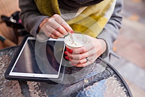 Girl stiring her coffee in the park. Tablet pc on the table. Close up.