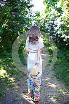 Girl in a straw hat with a blue ribbon on a spring afternoon. Back view. Trendy casual summer or spring outfit. Street fashion. Wo