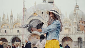 Girl in straw hat feeds pigeons on hand, San Marco. Famous ritual among tourists