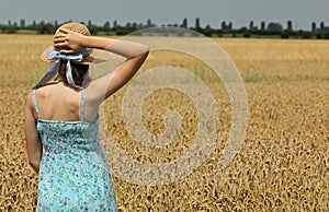 girl with straw hat looks at the ripe wheat field in summer