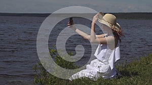 Girl in a straw hat photographing themselves on a mobile phone. Beautiful young woman photographed at the river