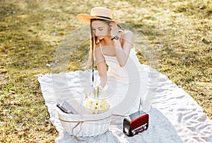 Girl with a straw hat in the spring in the park. Brunette with long hair sitting on a plaid on a background of summer nature.