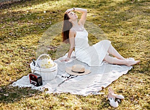 Girl with a straw hat in the spring in the park. Brunette with long hair sitting on a plaid on a background of summer nature.