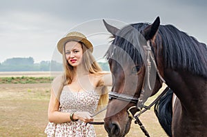 Girl in a straw hat and summer dress, posing with a horse