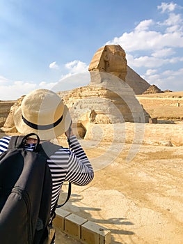 A girl in a straw hat takes pictures of Sphinx in Giza