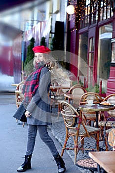 Girl in a gray coat with long curls is spinning near a cafe