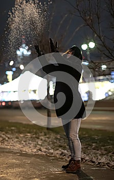 Girl on the street throws snow at night.