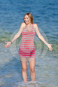 Girl in striped dress stands in water and laughs