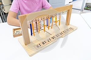 Girl in striped is playing and sorting a puzzle of colored plastic beads in montessori school