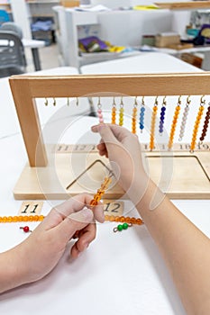 Girl in striped is playing and sorting a puzzle of colored plastic beads in montessori school