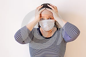 A girl in a striped sweater and medical mask in fear covered her head with her hands.