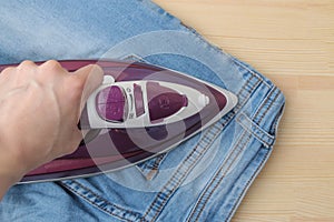 Girl strokes jeans. lilac iron and jeans. ironing clothes household electrical appliances. view from above
