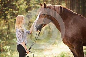 A girl stroking a horse in an autumn forest